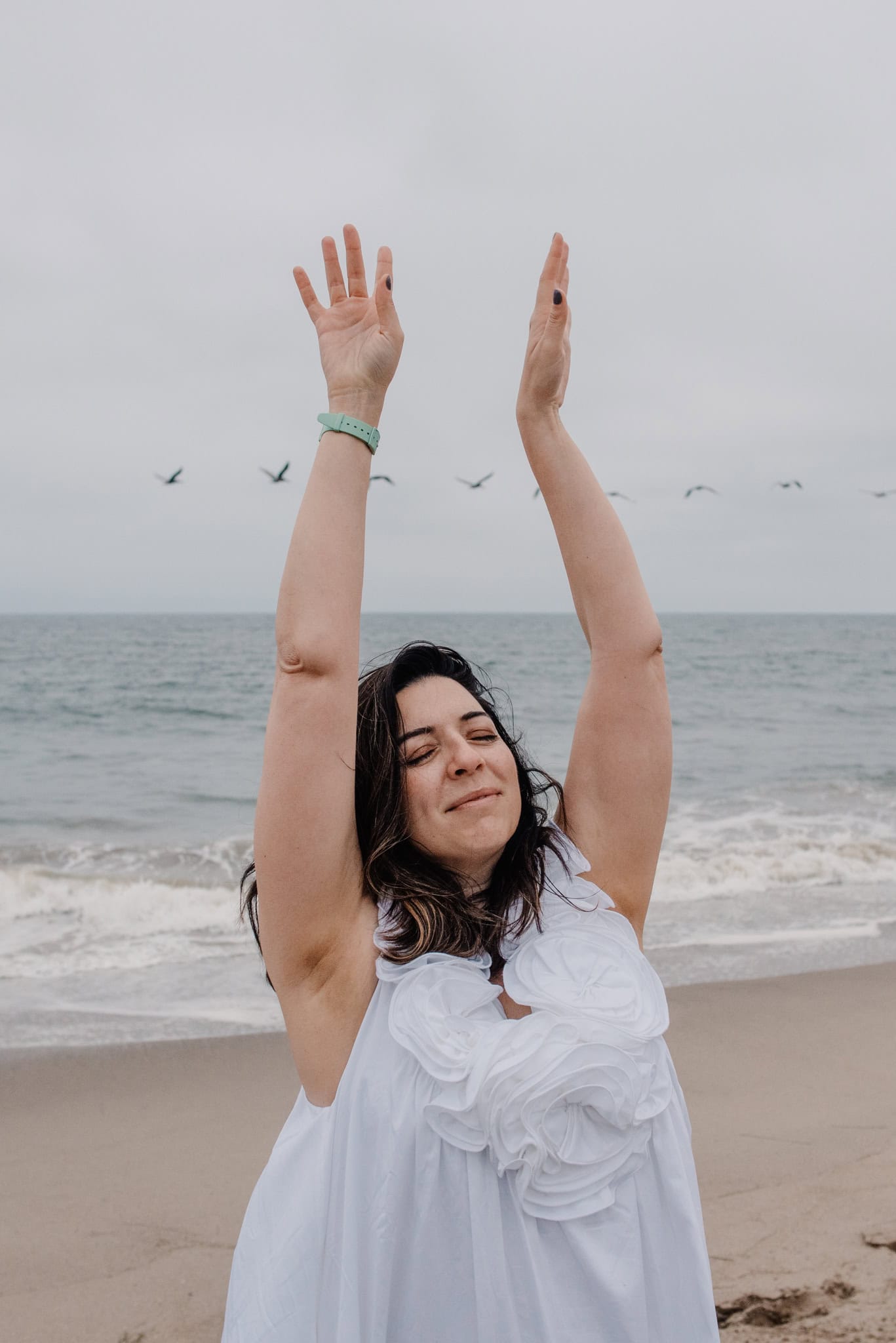 woman holding hands up with birds in the background during immersive art somatic experience near a beach