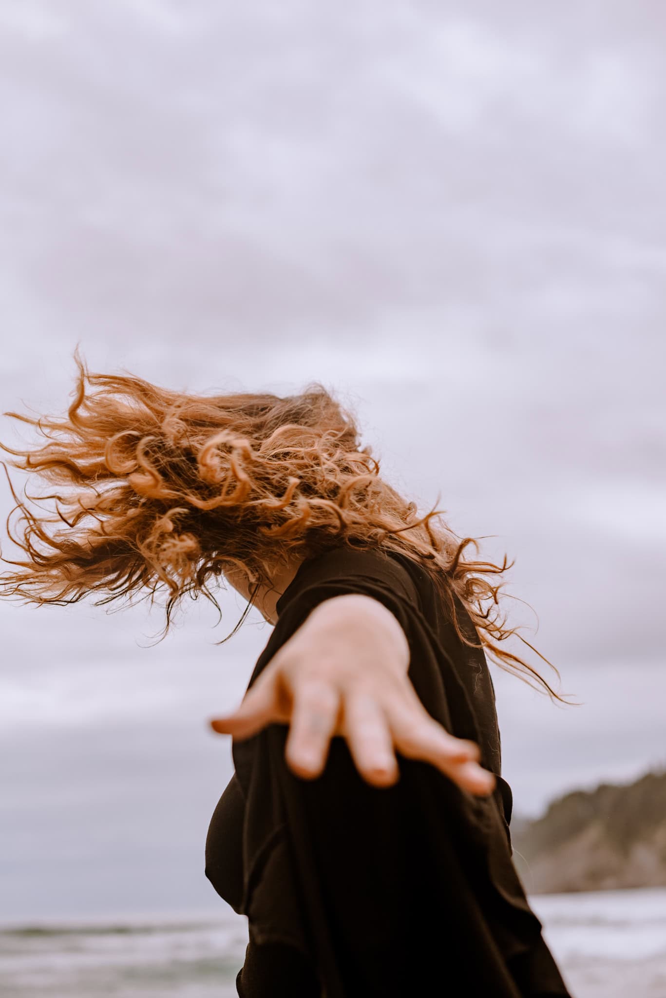 woman twirling hair out with hands out during immersive art somatic experience near a beach