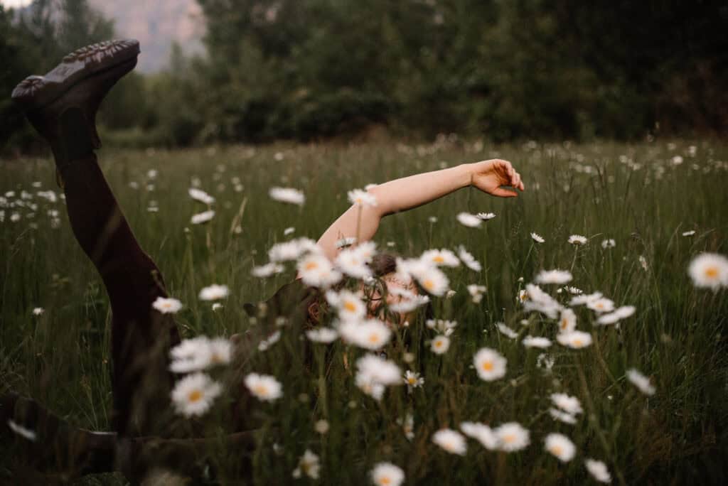 woman in a flower field with her legs up in an woman smiling in an aliveness experience